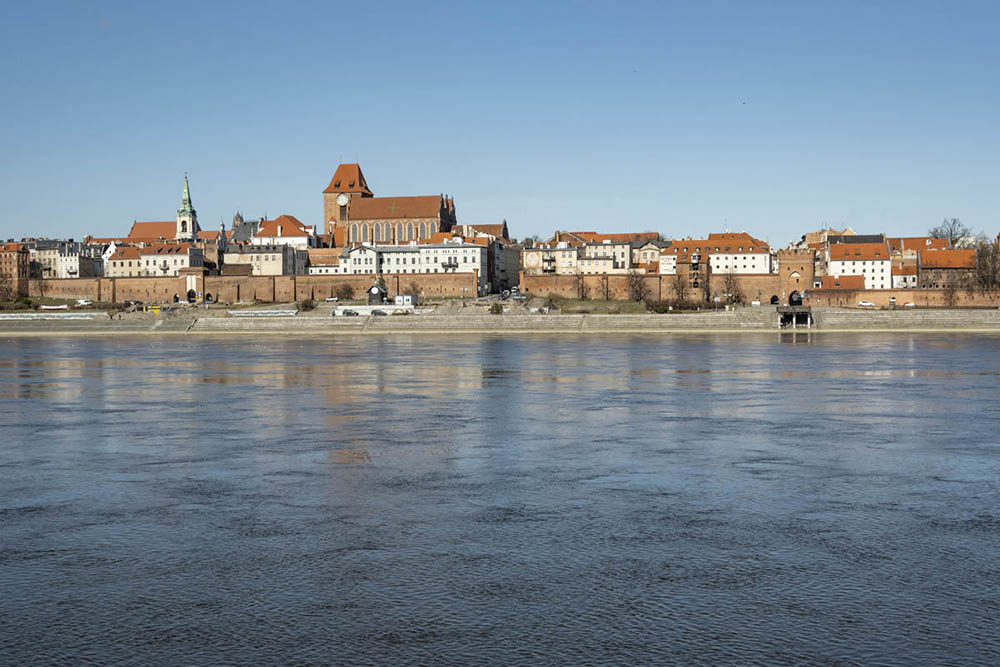 View of Torun from across the water: pretty cluster of medieval structures, with a wall along the river.