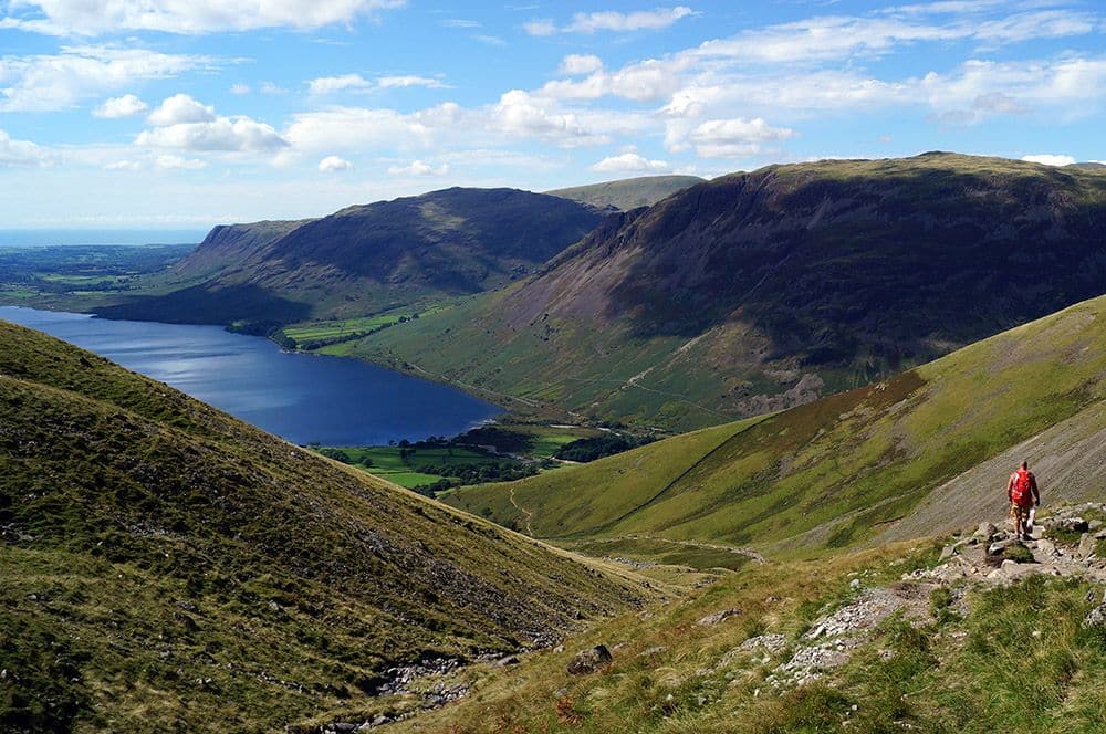 A view from up a mountain of a hilly landscape covered with low grasses, and a lake in a mountain valley in the English Lake District.