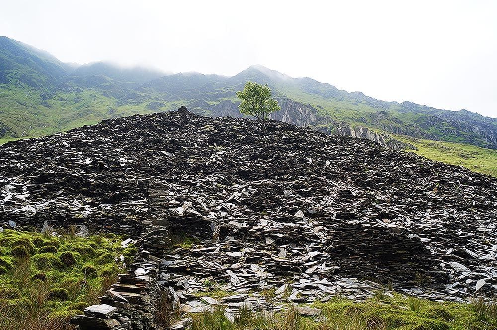 A hilly landscape with lots of loose slate pieces on the remains of a slate structure of some sort in Northwest Wales.