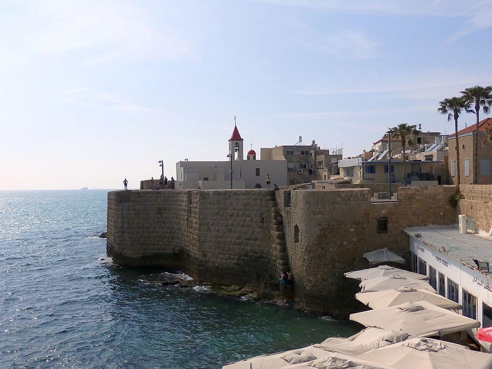 Acre Old City wall: The wall is stone and sits right on the edge of the sea. Above and inside it is a white church. 