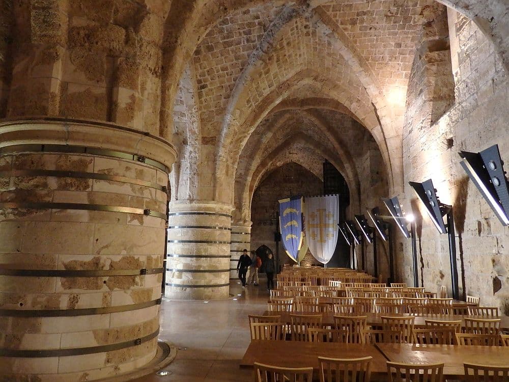 Acre Crusader fortress: Looking down a large hall with a wall on the right and enormous pillars on the left. Above, gothic arches.