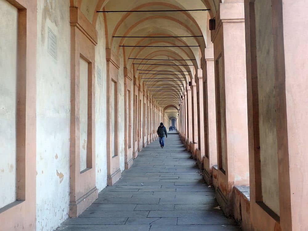 A long portico stretching ahead, the end point not visible. Just a couple of people walk on it in the distance.