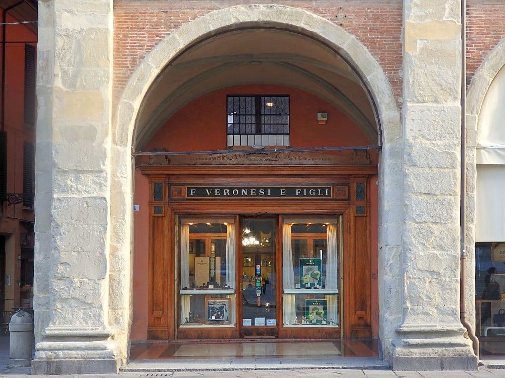 A storefront under a portico: a Romanesque arch frames the storefront, which fronted in brown wood with a central door and windows on either side of the door.