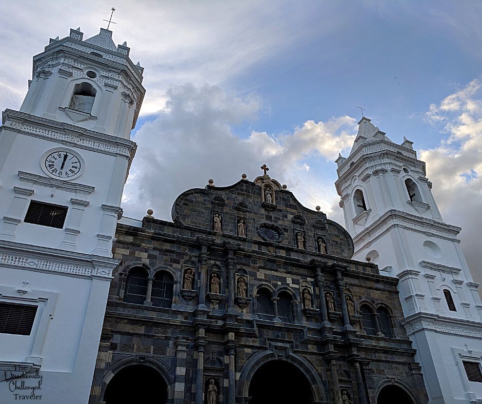 A church with a tower on either side in Panama Viejo: the towers are painted white while the church is natural stone, but with ornate stonework decorations.