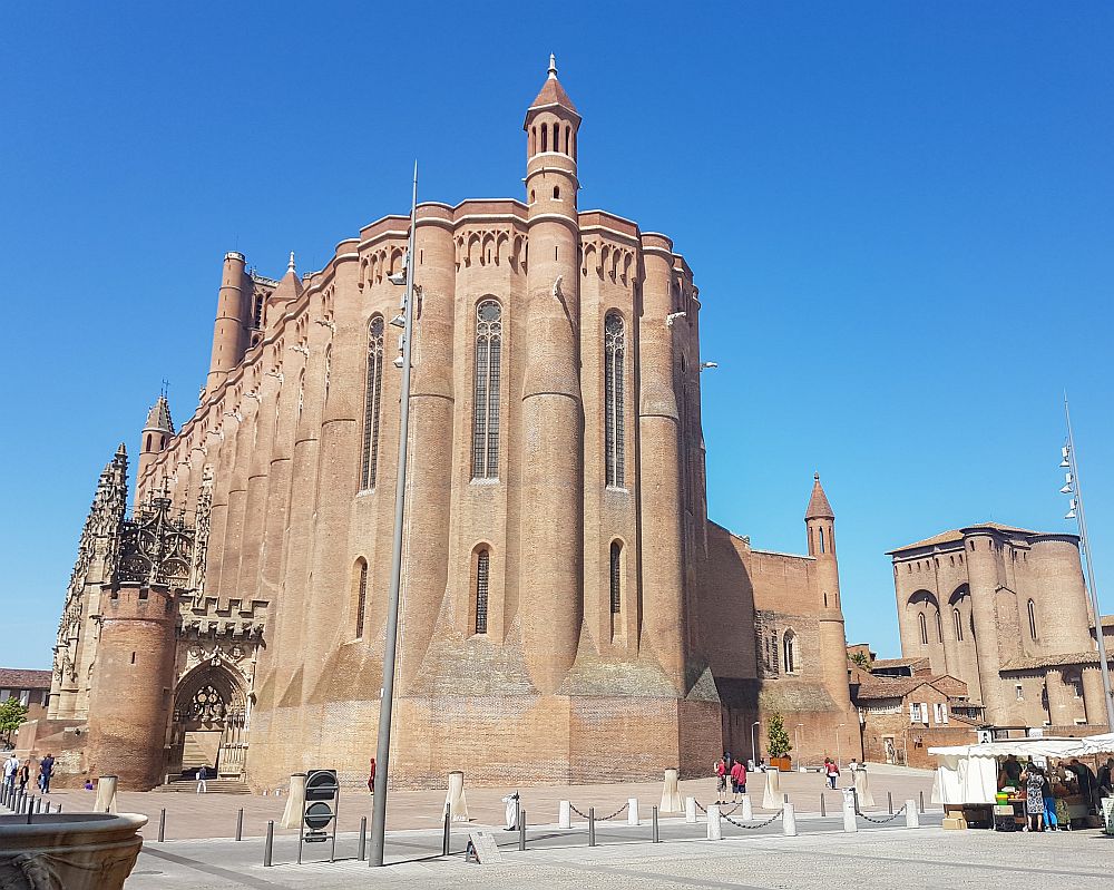 The Albi cathedral: a rather plain red-brick exterior, with simple walls and rounded towers not much higher than the main body of the cathedral. Tall narrow windows.