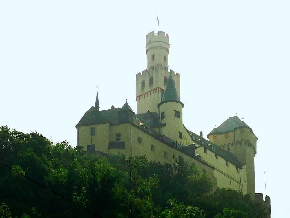 Looking up at a castle on a hill in the Upper Middle Rhine Valley: it's white with a tall square tower.