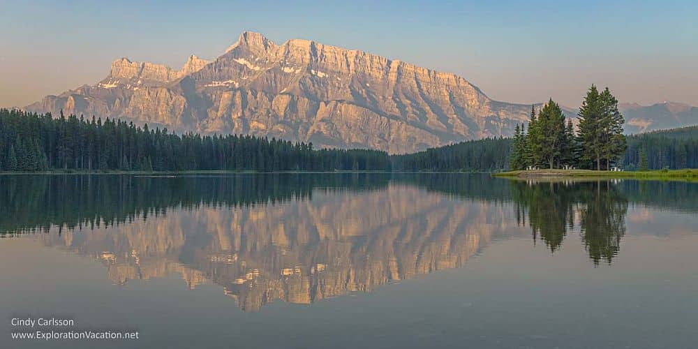 Canadian Rocky Mountain Parks: a still lake shows a reflection of the steep bare-rock mountain behind it.