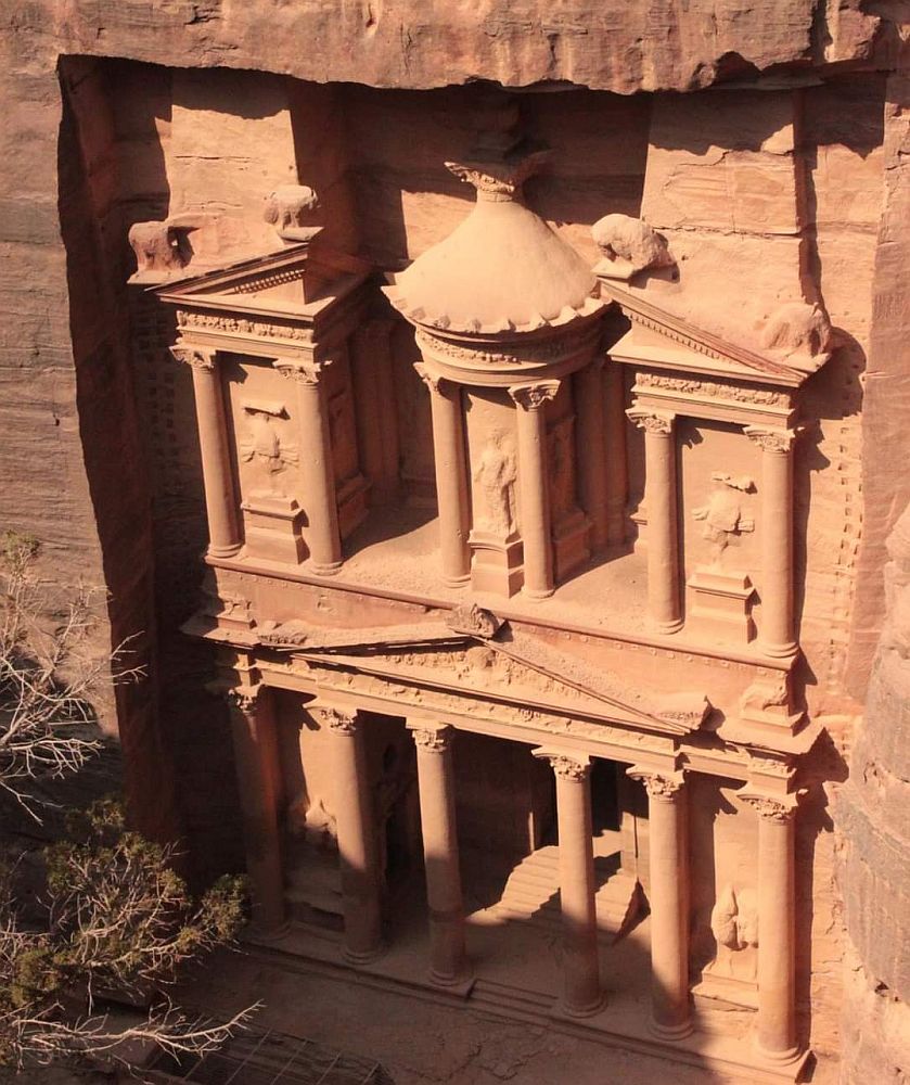The Treasury in Petra seen from a bit above it. It looks like an ornate 2-story temple, but it is cut right out of the side of a cliff in reddish sandstone.