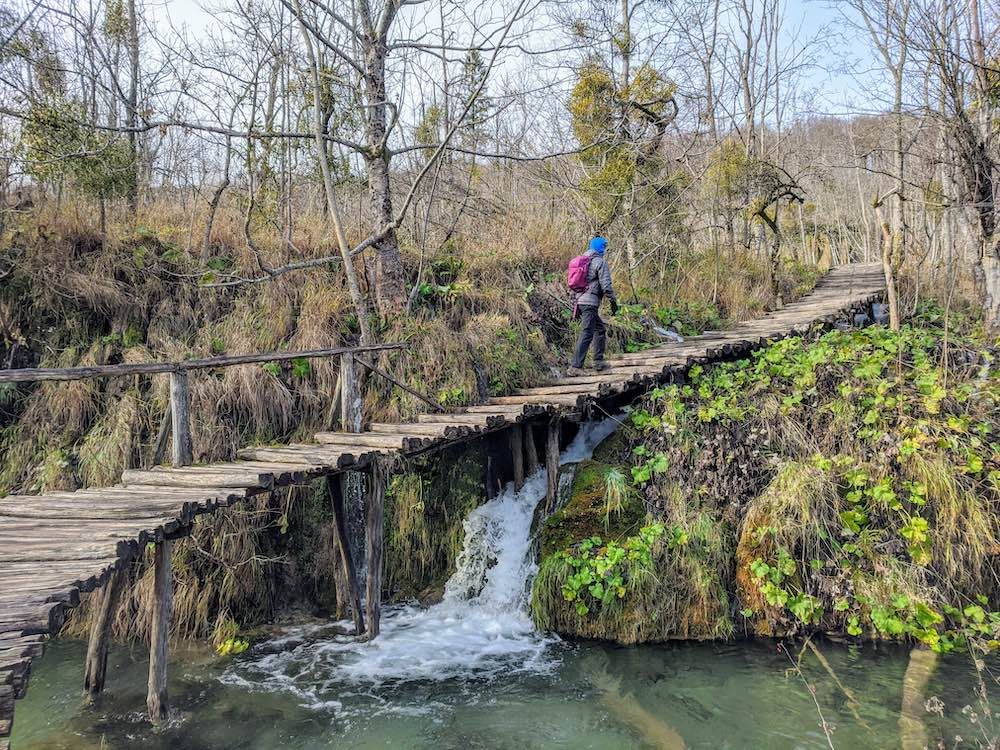 A person follows a wooden boardwalk over a waterfall at Plitvice.