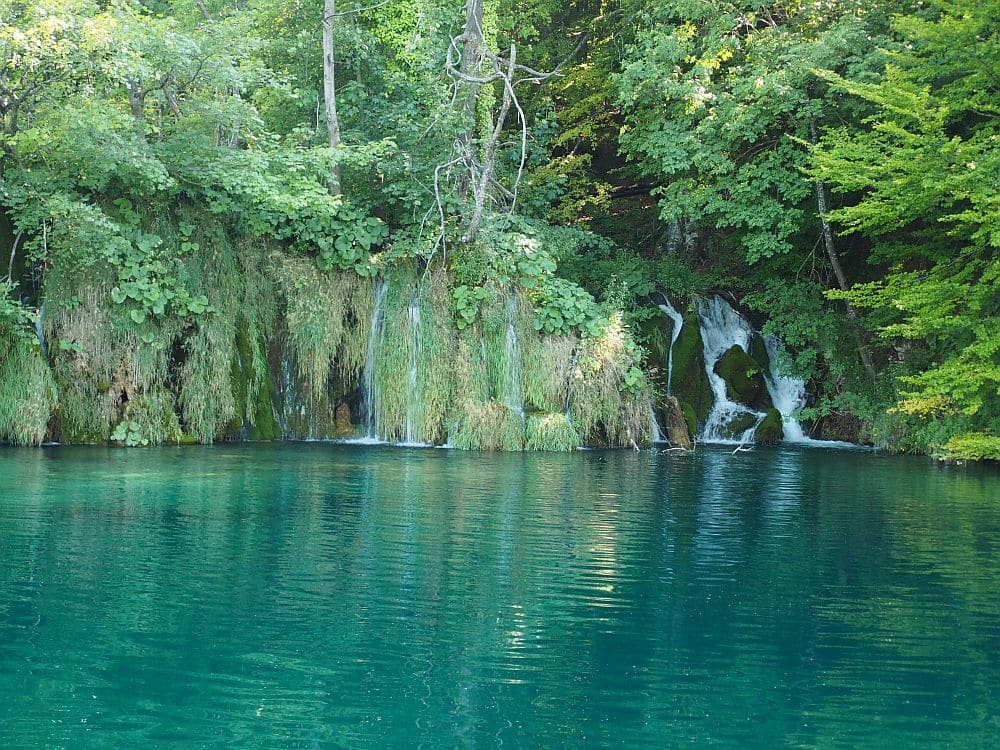 A lake of blue water with a number of waterfalls tumbling into it from amid the greenery.