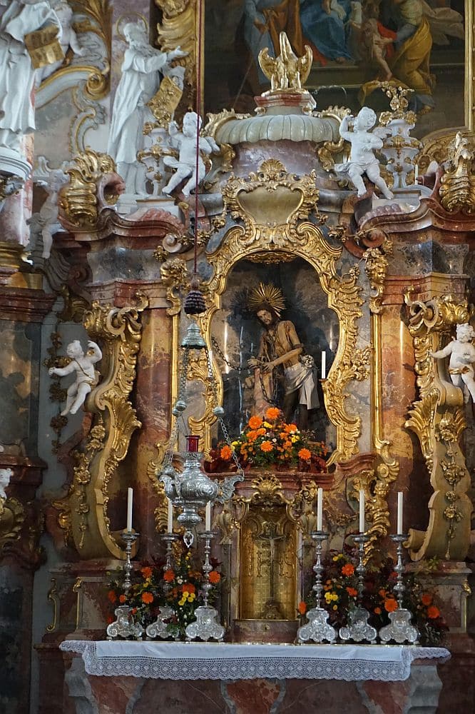An extremely ornate section of the altar at the PIlgrimage Church of Wies. The decorations - mostly gold - surround a small statue of a standing chained Jesus.
