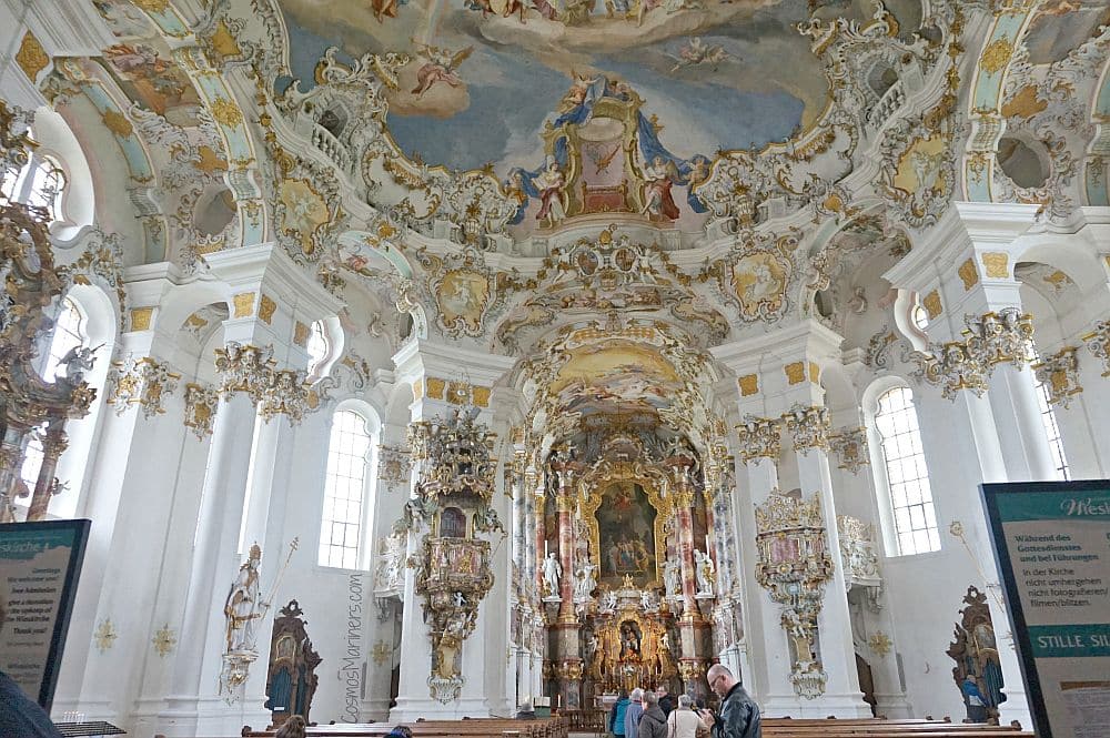 Looking toward the altar in the Pilgrimage Church of Wies: richly decorated with gold and paint on white walls. The decorations cover the ceiling as well, and the altar is predominantly gold.