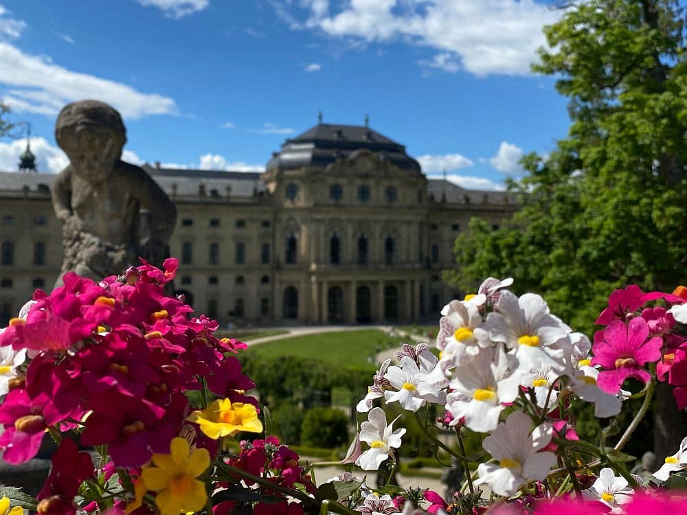 Brightly-colored flowers in focus in the foreground, the Wurzburg Residence blurred in the background.