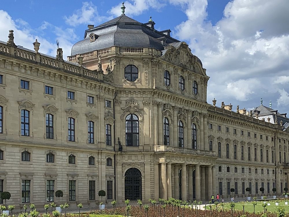 A view from an angle of the grand entrance to the Wurzburg Residence, with a domed roof, and arched doors and windows extended forward from the rest of the building.