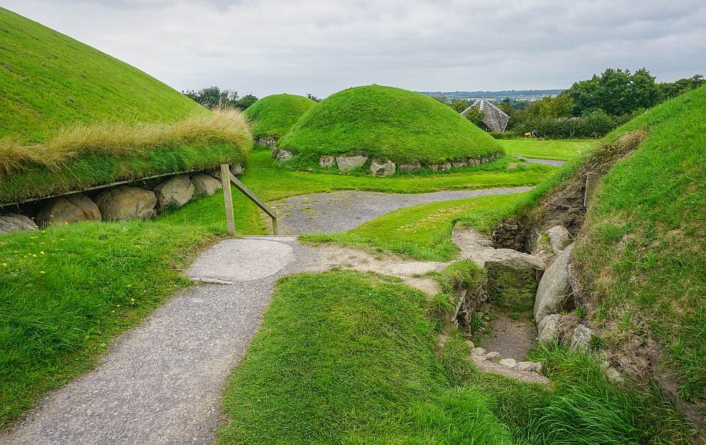 A walkway with mound-like structures on either side: stones on their sides, covered in grass on their tops.