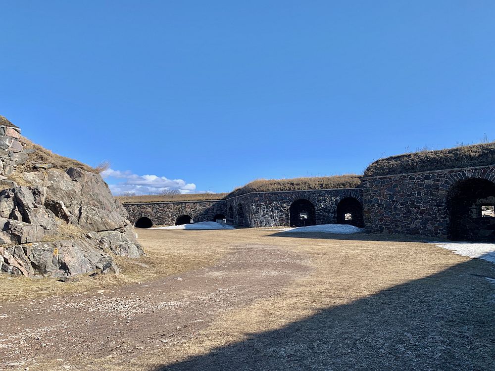 A flat area inside a series of walls seen in the distance, which have dark entrances visible.