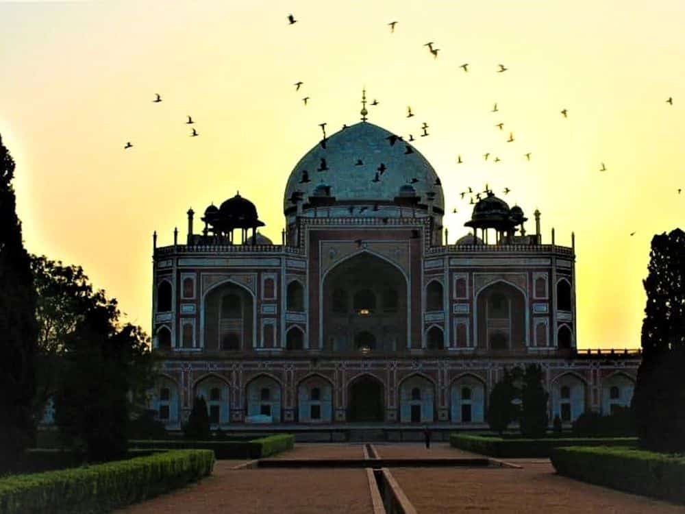 The tomb at sunset or sunrise: it is almost a silhouette against the bright yellow sky, and a flock of birds flies across.