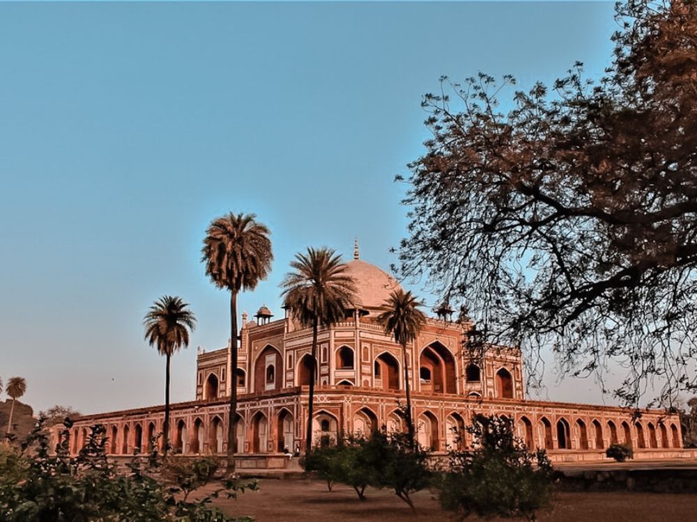 View of Humayun's tomb from an angle: the ground floor is much larger than the upper floors, which rise from the center, with a central dome.