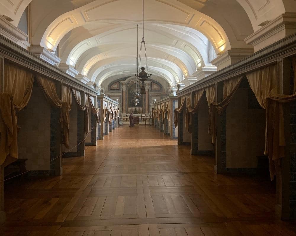 A long hall with an arched roof. Along the sides, curtains pulled aside at openings to side rooms.