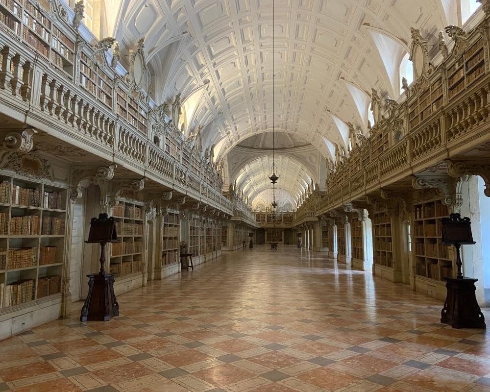 A long empty hall with an arched roof and windows along the ceiling. Below the windows, bookshelves filled with books.