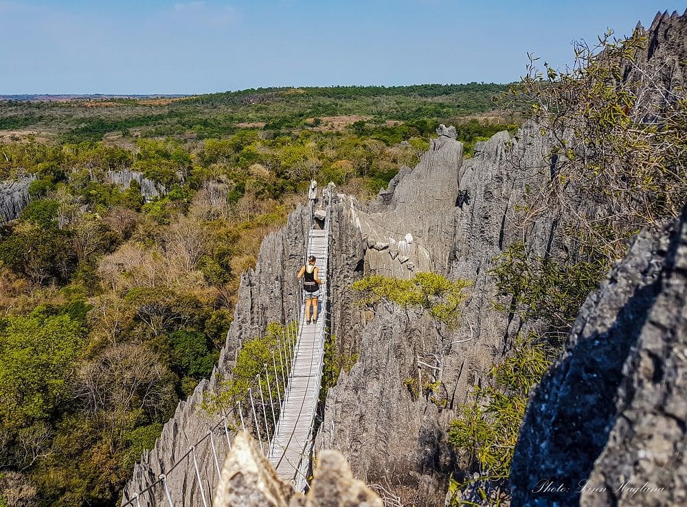 Granite cliff with a bridge strung between two pinnacles: the bridge has rope or cable rails, and the floor is wooden planks strung together. A person walks across it.