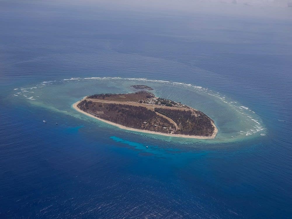 Lady Elliot Island seen from the air: oval shaped, with scrubby growth, a few buildings, and what looks like a dirt airstrip straight across its middle.