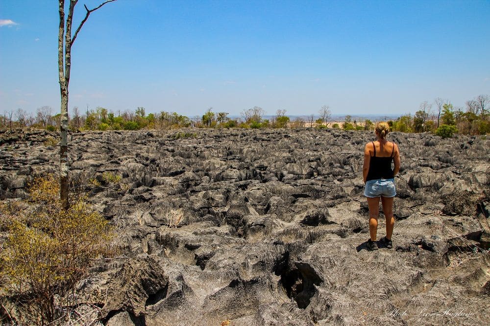 Image. A person stands on a ledge overlooking a very bumpy area of granite.