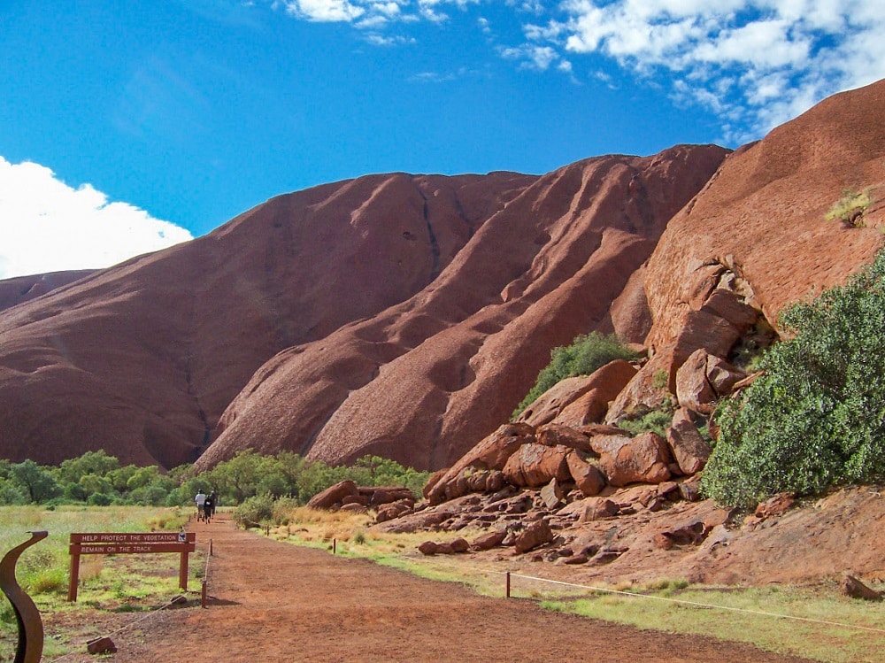 A dirt path skirting the edge of the wall of rock that is Uluru.