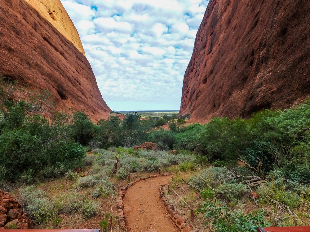 A dirt path cutting between the steep sides of two dome hills at Kata Tjuta.