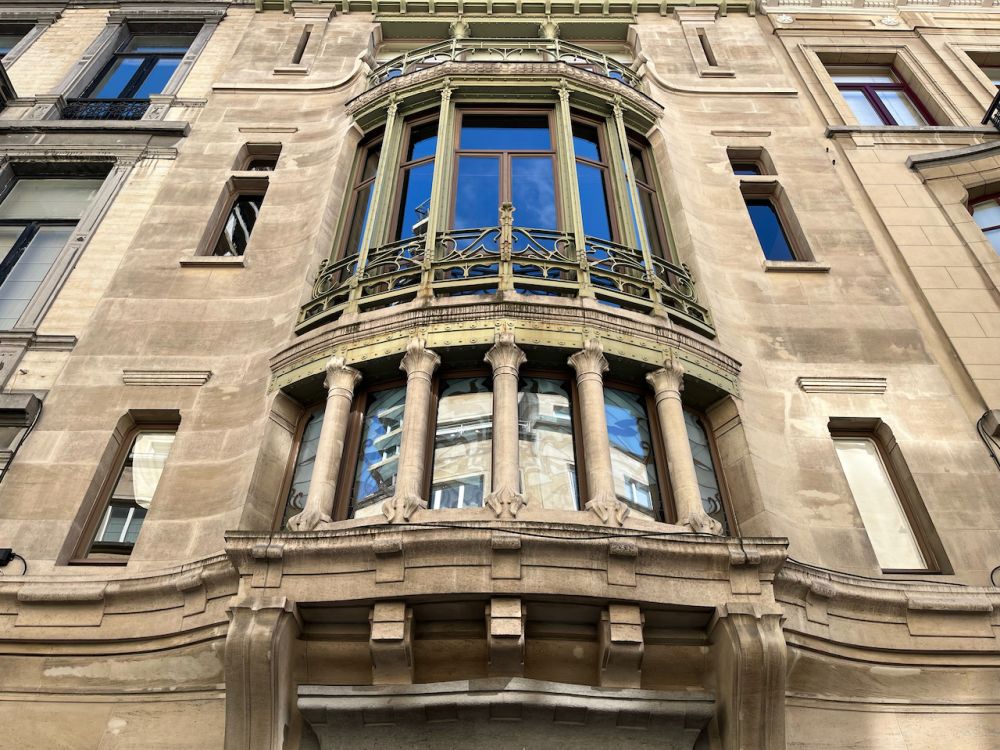 Looking up at the facade of the building, with a 2-storey high rounded section with long rectangles of glass and decorative pillars.