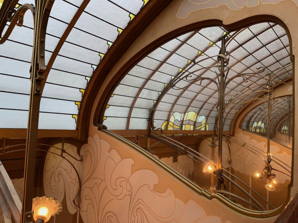 An arched ceiling, mostly made of rectangles of glass. The arches supporting the glass are in a typical art nouveau style.