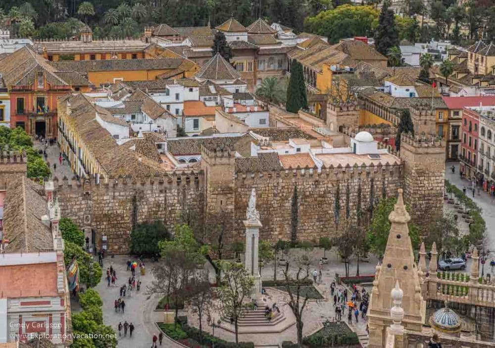 An aerial view of the Alcazar: Large stone walls with crenellations and towers surrounding a tightly-packed cluster of buildings.