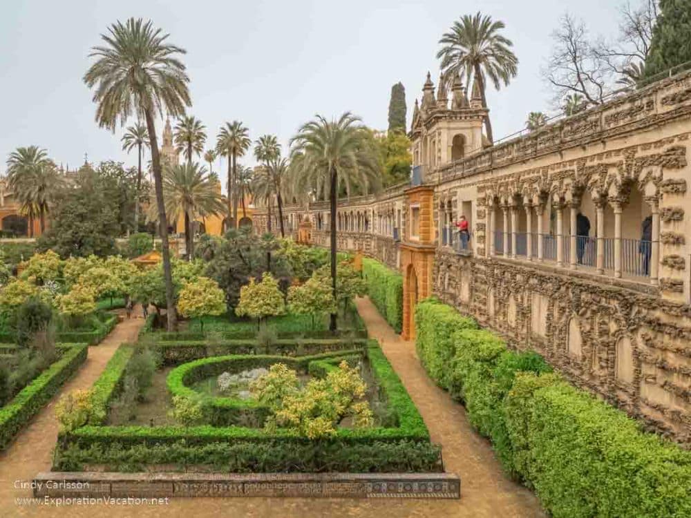 A view down the side of the Alcazar on the right, with the gardens straight ahead: formal, neatly trimmed hedges in squares and the occasional palm tree.