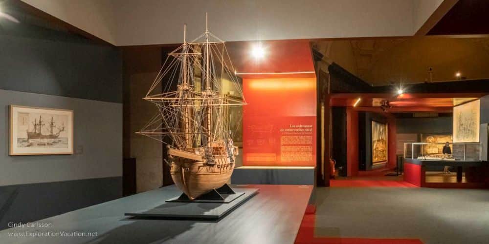 A modern exhibition space with a model ship on the left and images and text on the walls.