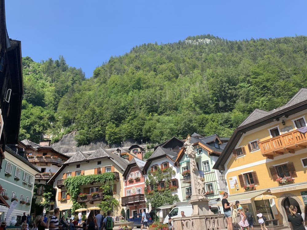 A row of typical Austrian buildings on an open plaza, with a forest-covered mountain rising behind them.