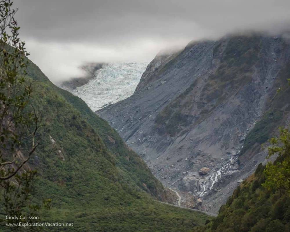 Looking down a valley between mountains; in the distance, a glacier on the side of a mountain.