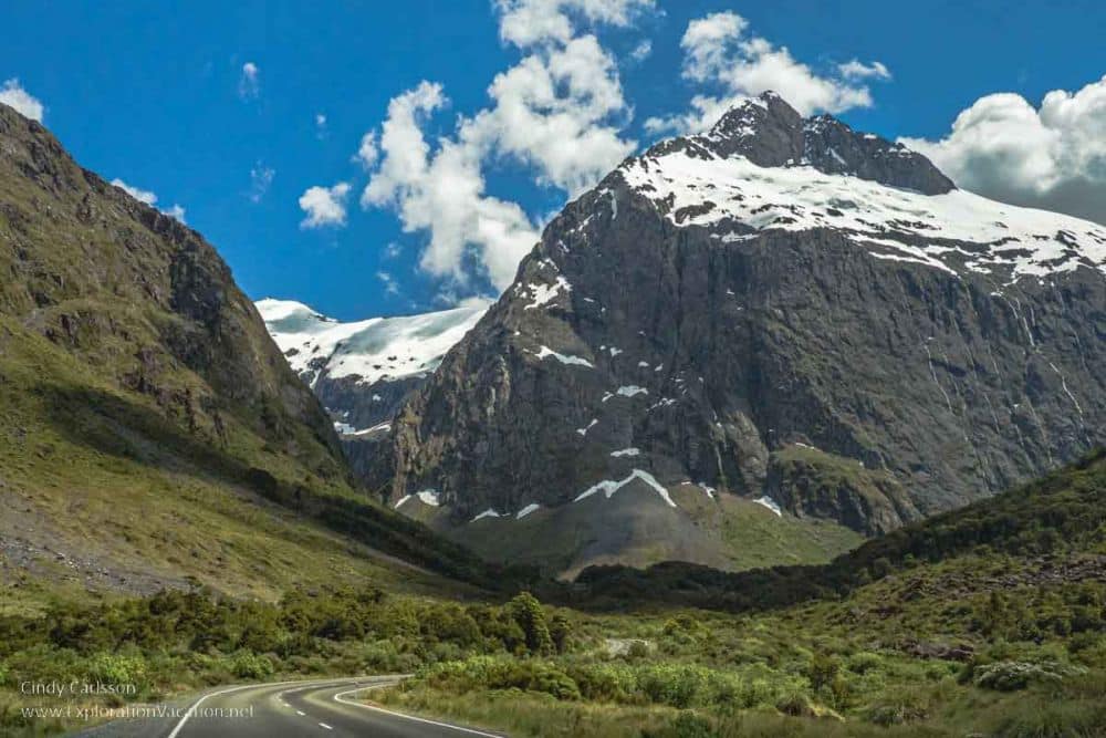 A road curves away into the distance, where tall mountains rise.