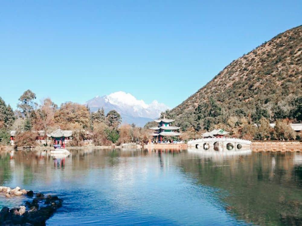 Seen across a pond, a pagoda stands on the shore in front of a hill.