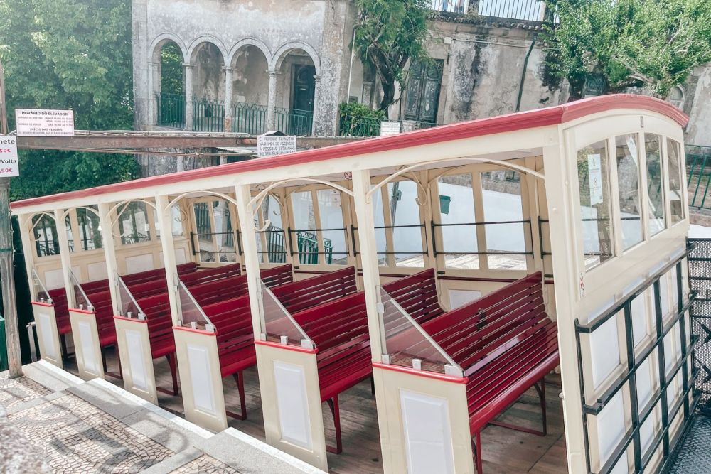 The funicular, parked on a slope, has red benches, open on the sides.