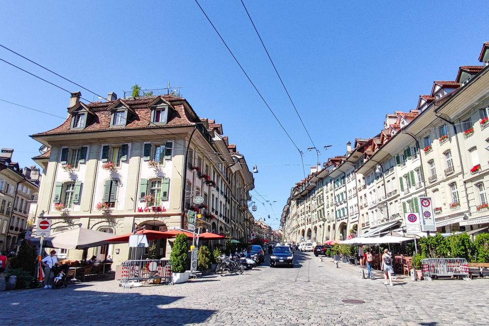 View of a plaza and looking down a cobblestone street lined with 4-story buildings, shops on the ground floors.