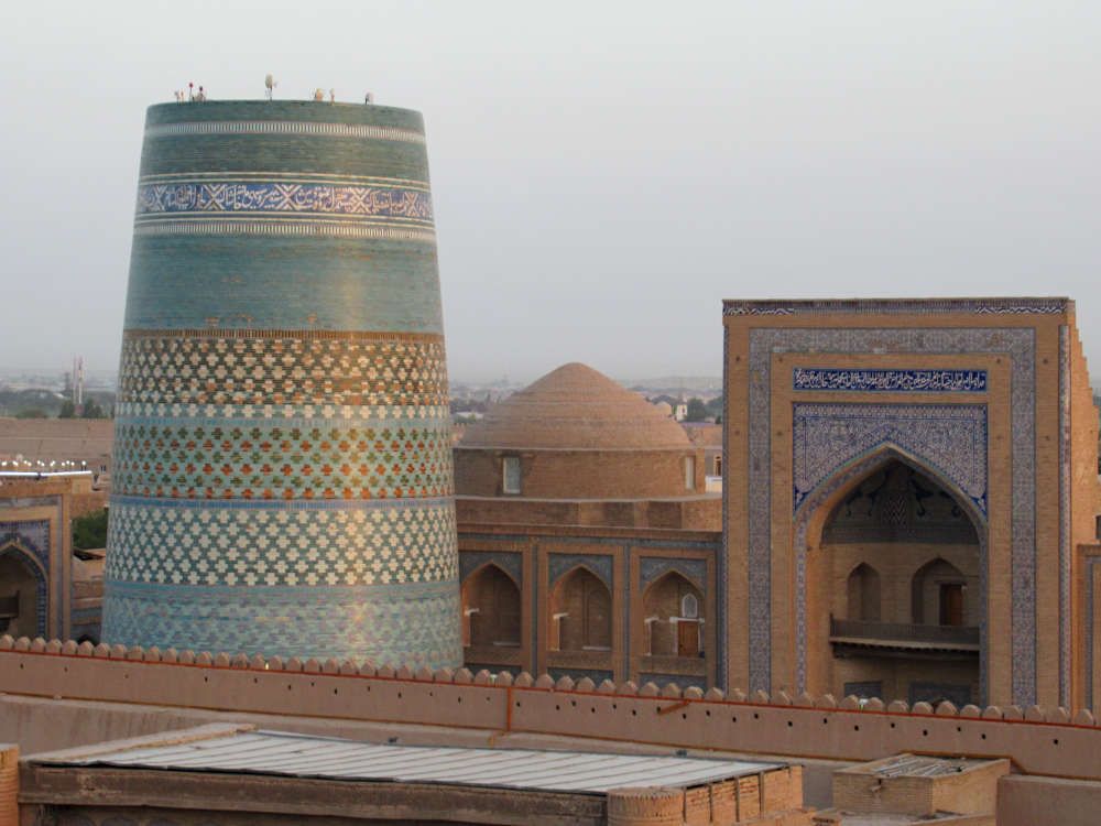The unfinished minaret has decorative bands around it. It is unfinished, yet considerably taller and wider around than the mosque visible beside it.