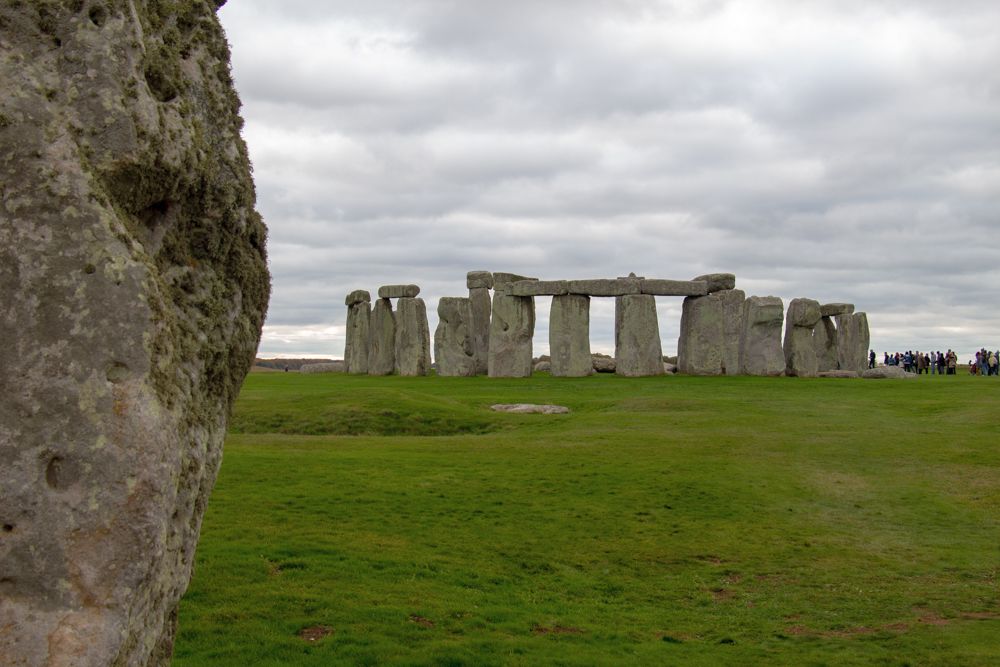 A view of the stone circle of Stonehenge, seen across a flat grassy field.