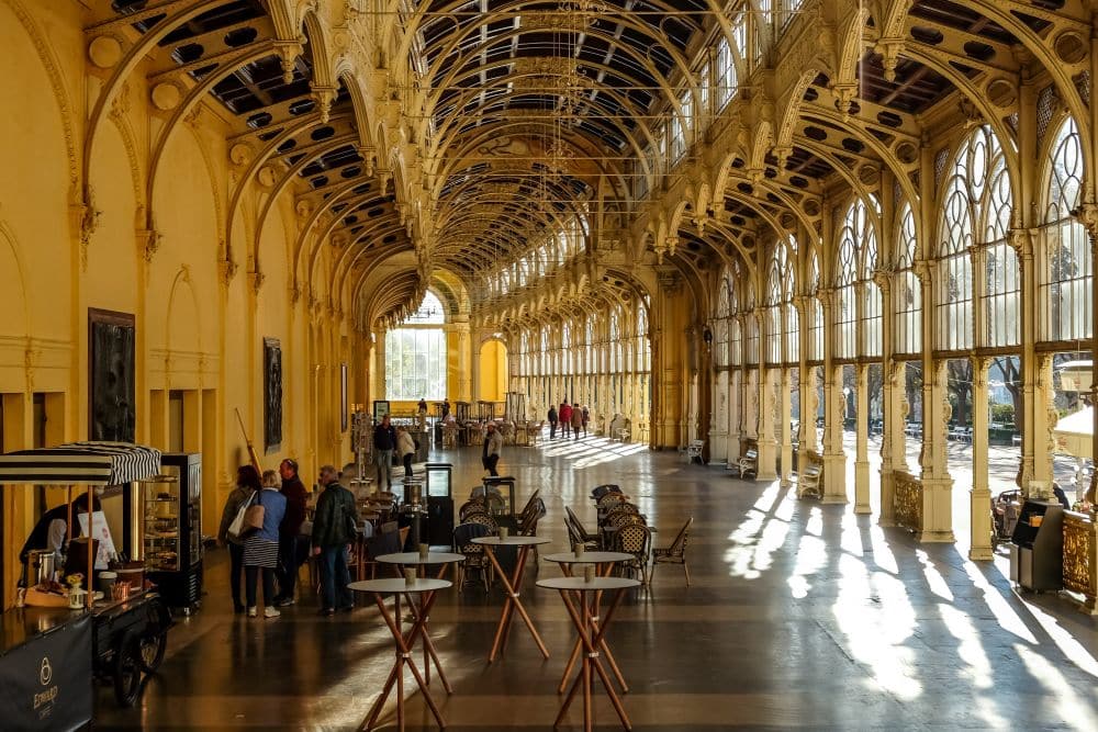 Interior view of the colonnade: a long slightly curved hallway, quite wide, with a building on the left and arches on the right to the outdoors.