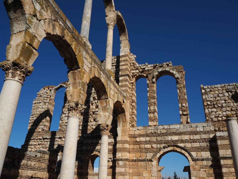 Fragmentary walls with striped stonework: stone alternating with brick. Pillars support skeletal arches.