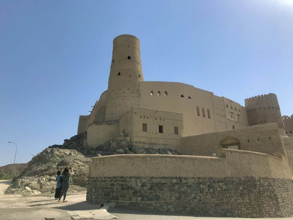 The imposing fortress on a small hill: mud walls and a tall round tower at its corner.