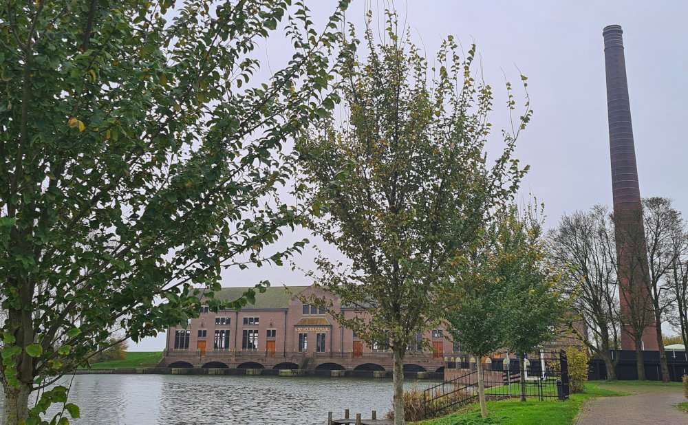 A view of the main brick building - wide and low over the water - and a very tall brick chimney next to it.