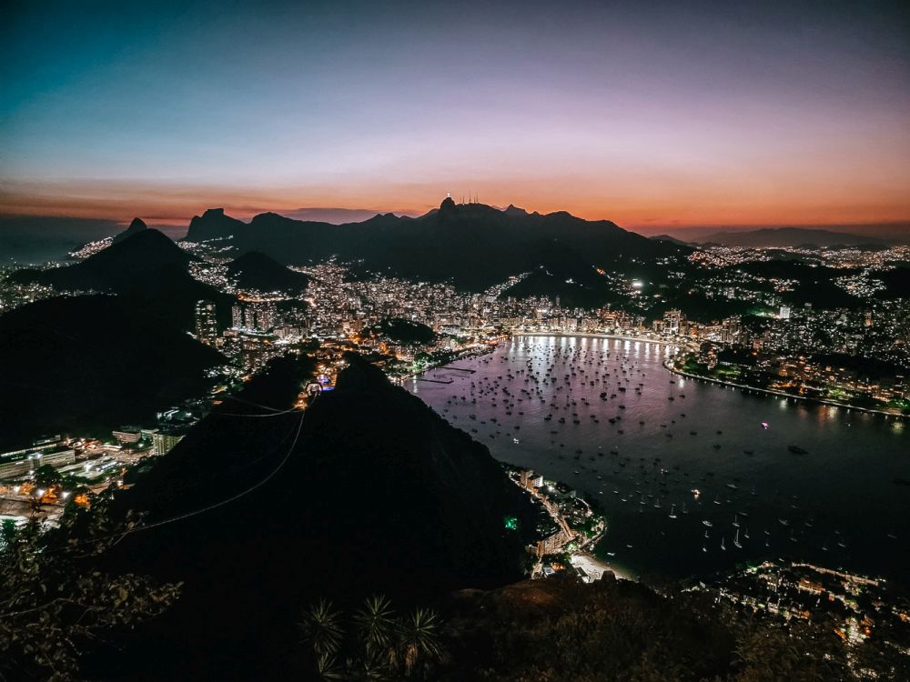 The mountains are black against a post-sunset sky, but the lights of Rio de Janeiro surround and climb the sides of the mountains and shine on the water.