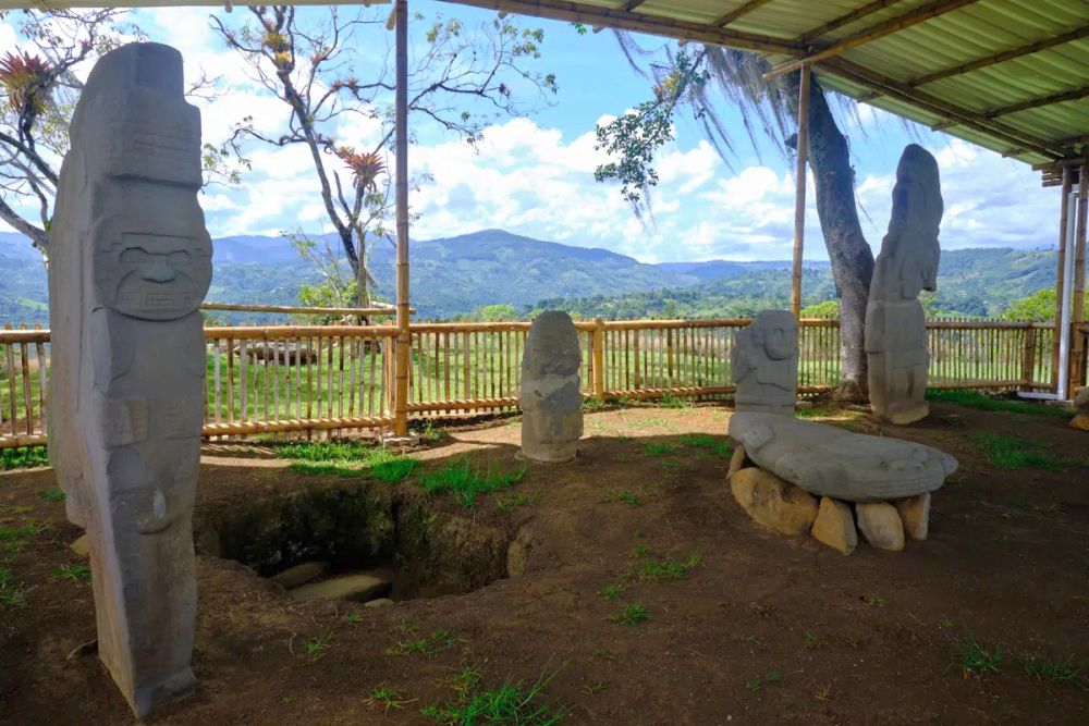 Under a sheltering roof, several statues as well as a pit with, behind them a wide view of valley and mountains.