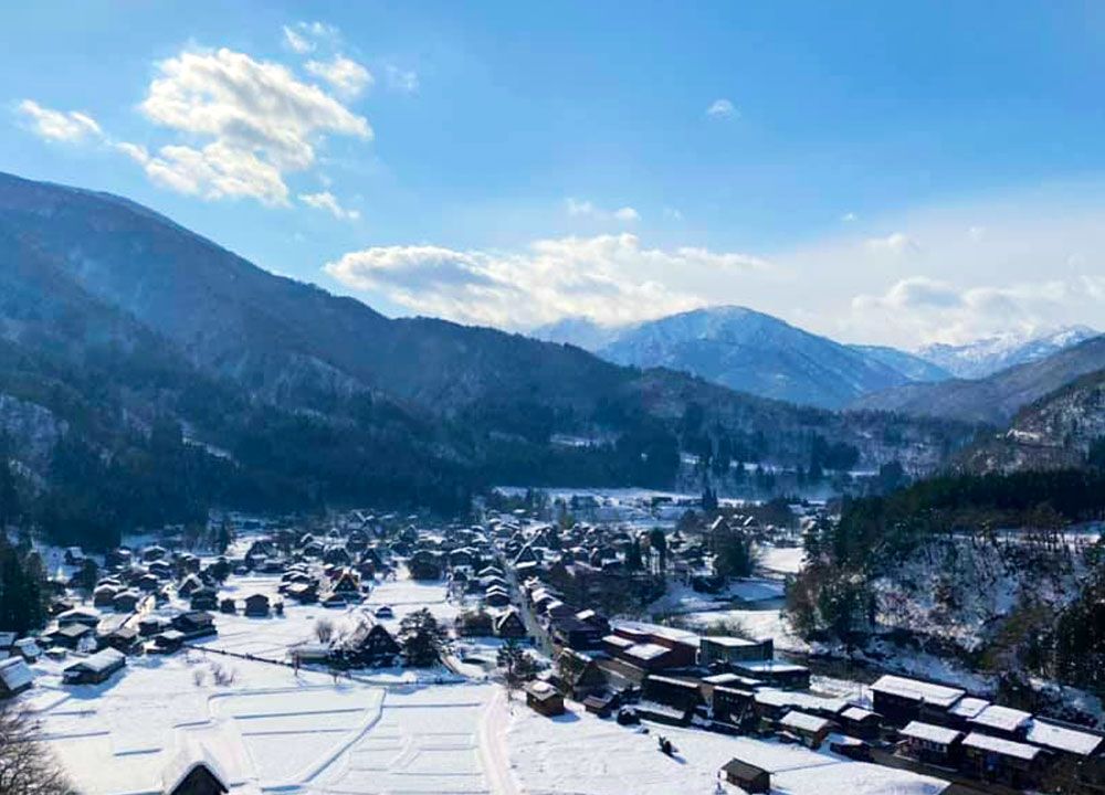 A view over Shirakawa-go village, snow-covered and surrounded by mountains.