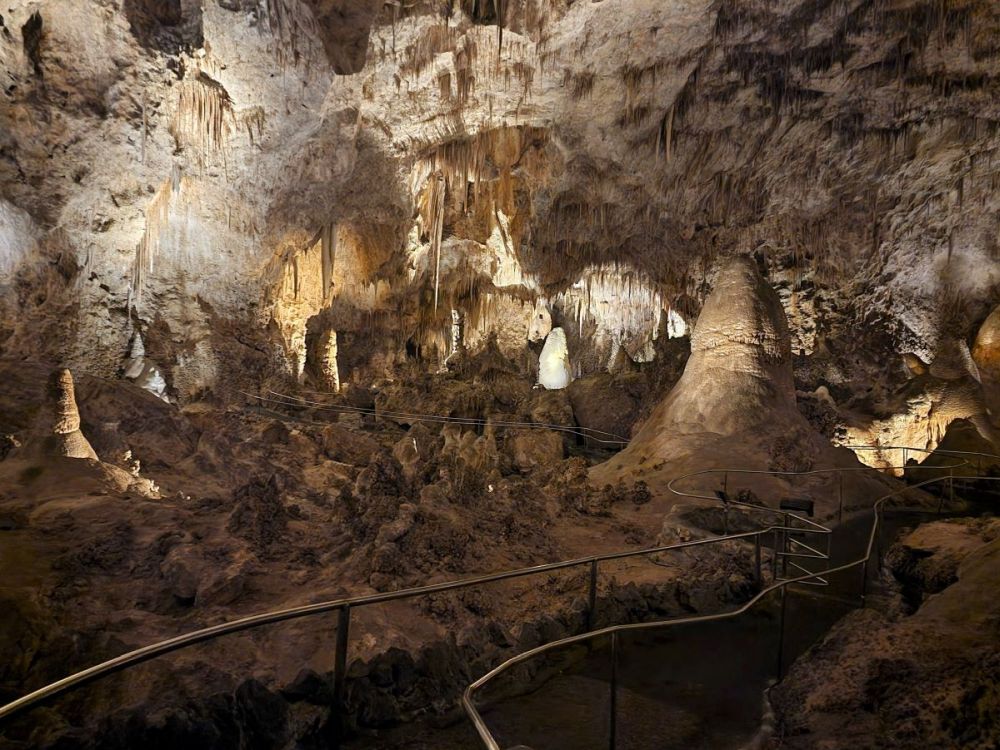 A view of a cave with stalactites and stalagmites and the railings of a pathway are visible winding among them.